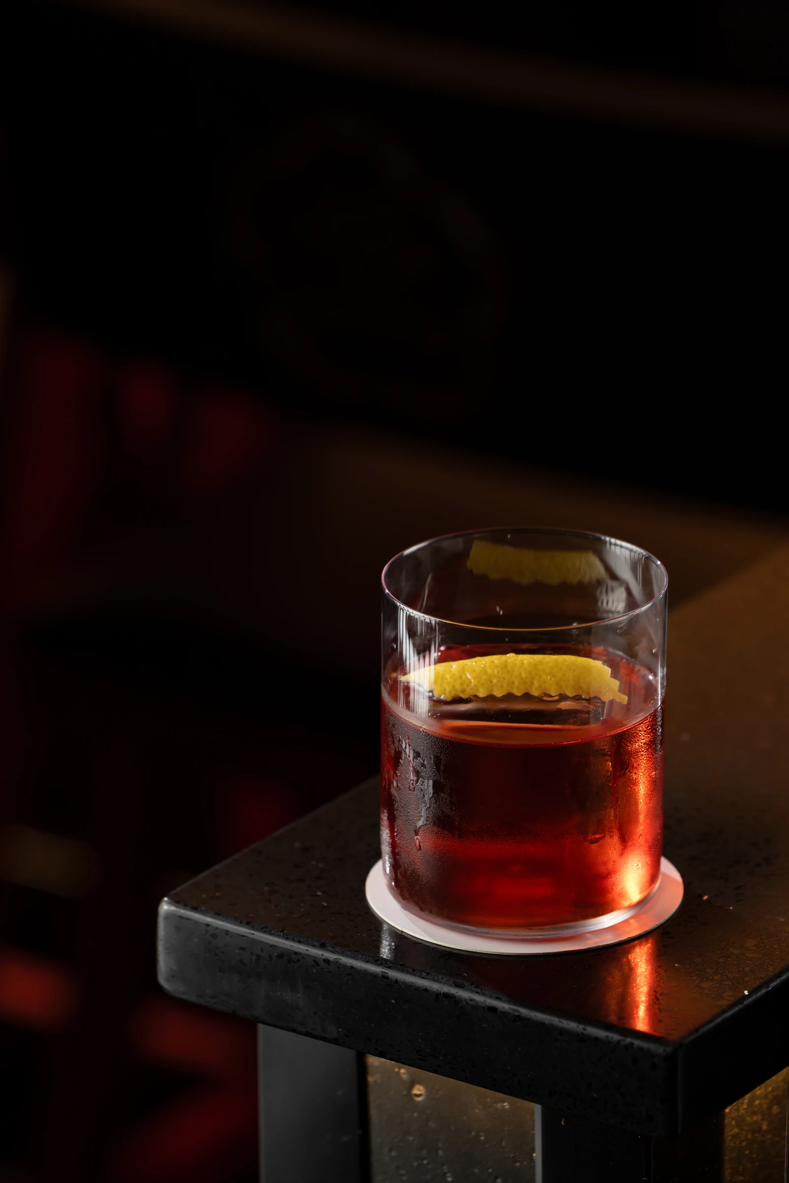 Deep red cocktail over ice with a citrus peel in a rocks glass
