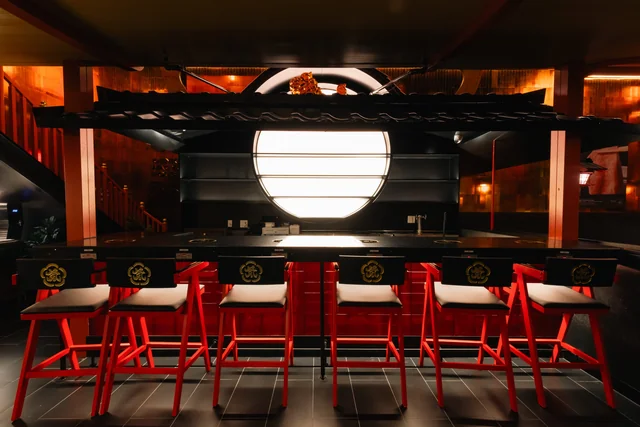 Counter seats with red stools beneath a glowing round window at Genki Wagyu House